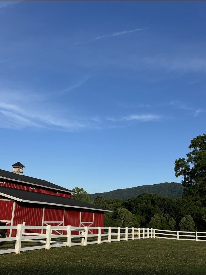 Red barn, white fencing, and mountain view under a blue sky
